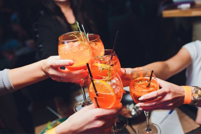 Personas levantando copas con bebidas naranjas, celebrando juntas en una reunión social.