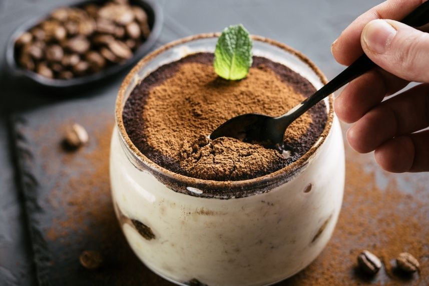 Postre de café y chocolate con una cuchara al lado, presentado en un plato elegante.