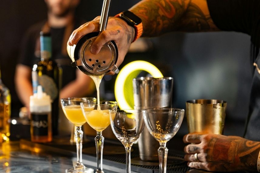 Un bartender de Sibari Medellín vierte cuidadosamente un cóctel en un vaso, resaltando su habilidad.
