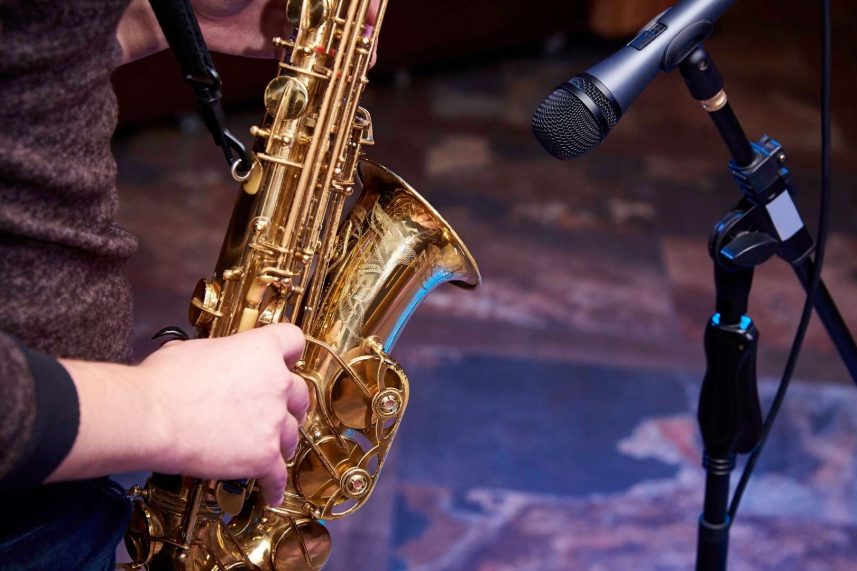 Persona tocando un saxofón frente a un micrófono en un escenario iluminado.