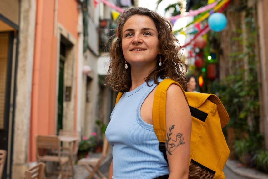 Mujer con mochila de pie en una calle estrecha, rodeada de edificios altos y un ambiente urbano.