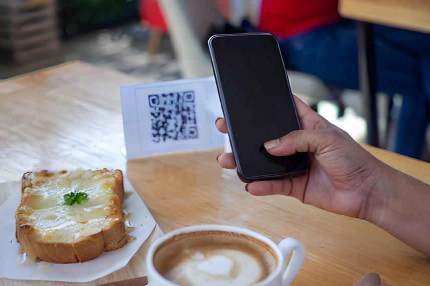 Persona sosteniendo un teléfono celular junto a una rebanada de pan sobre una mesa.