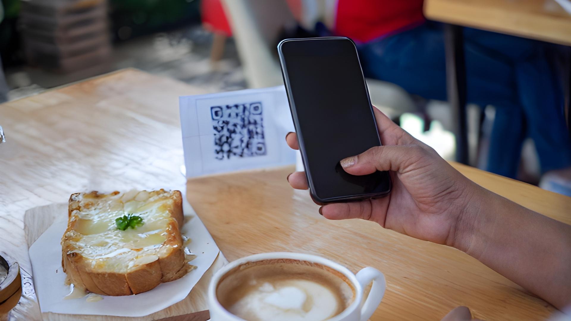 Persona sosteniendo un teléfono celular junto a una rebanada de pan sobre una mesa.