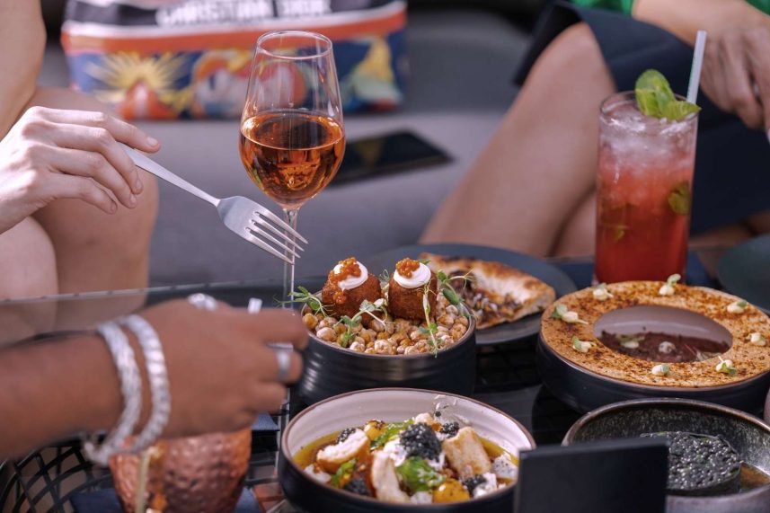 Varias personas compartiendo una comida y bebidas en una mesa, creando un ambiente de camaradería.