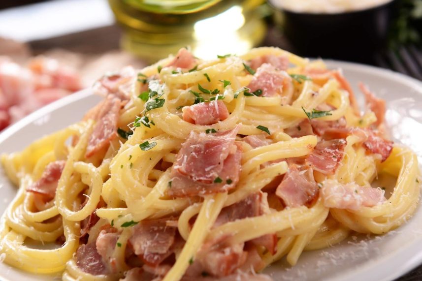 Un plato de espagueti cubierto con jamón y queso, listo para servir, con un fondo de mesa de madera.