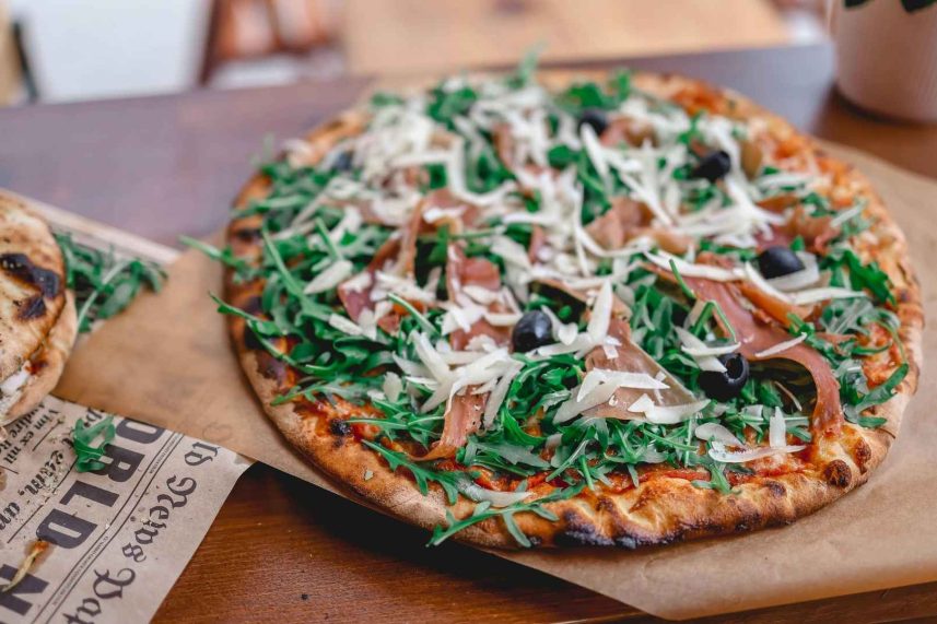 Pizza sobre una mesa de madera acompañada de una copa de vino.