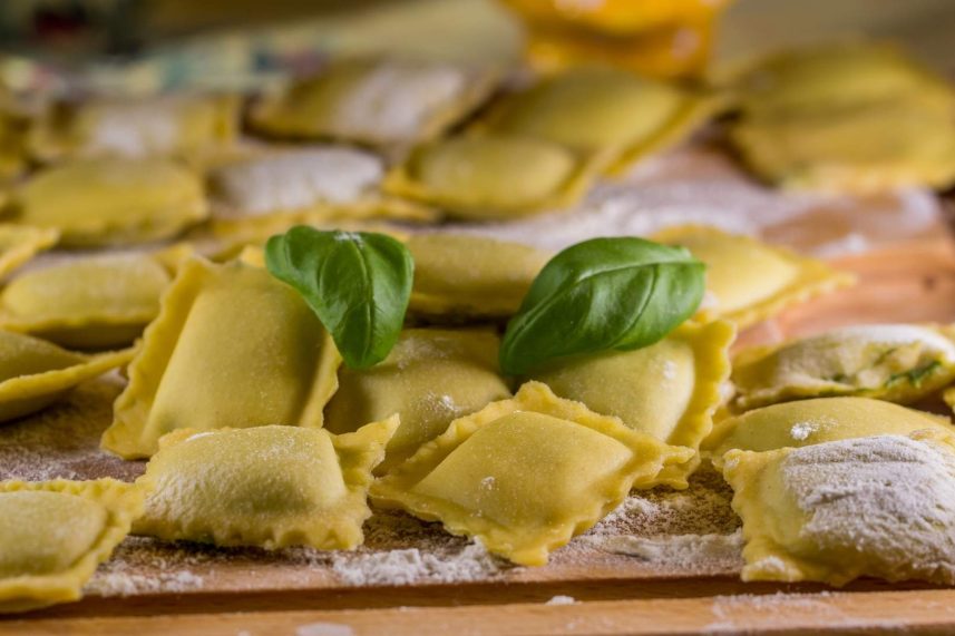 Tabla de cortar de madera con raviolis frescos y hojas de albahaca.